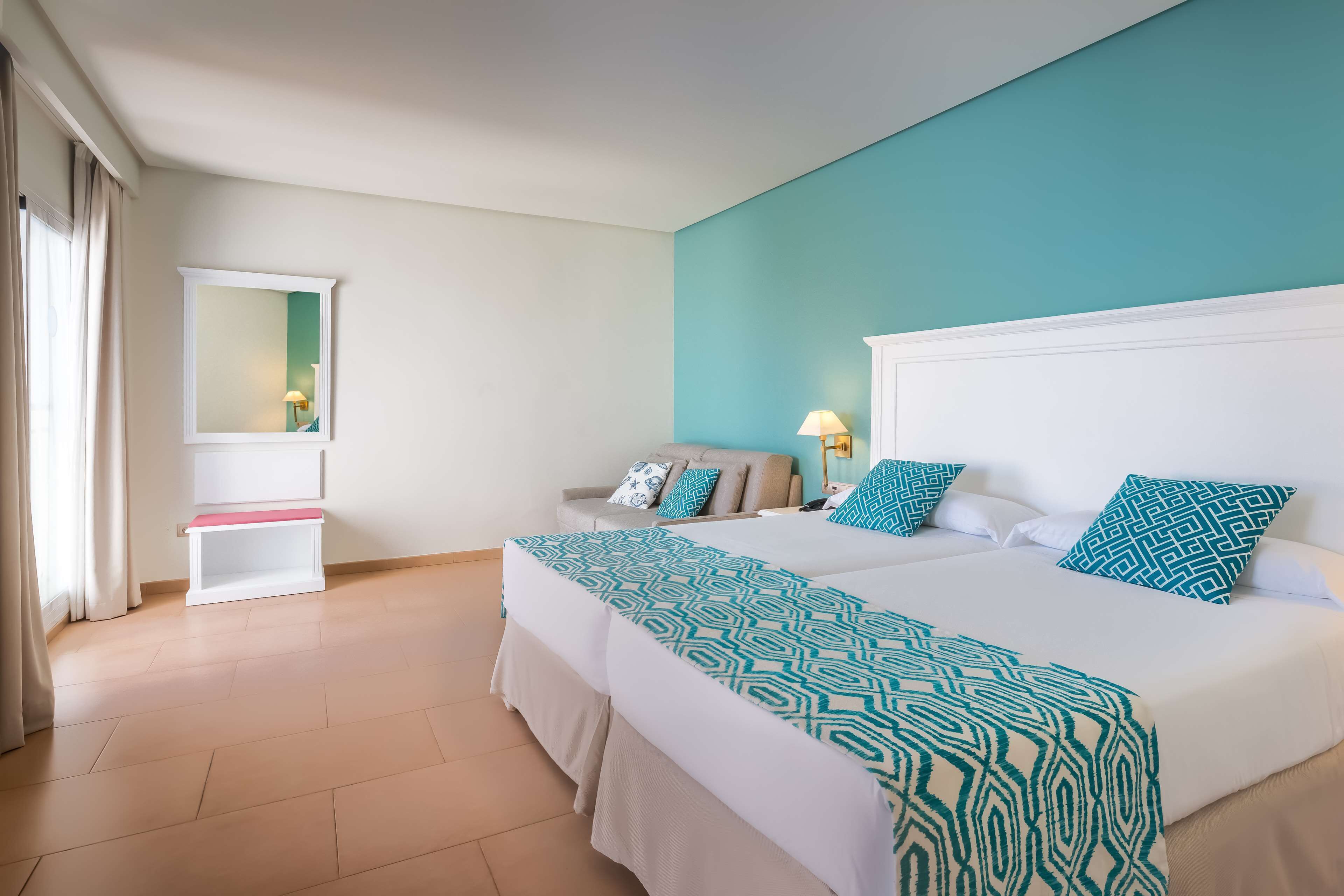 A hotel room with two beds, a sofa, a small table, and a mirror.