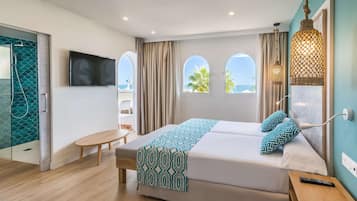 Een moderne hotelkamer met een groot bed, een televisie, een bankje en uitzicht op zee.