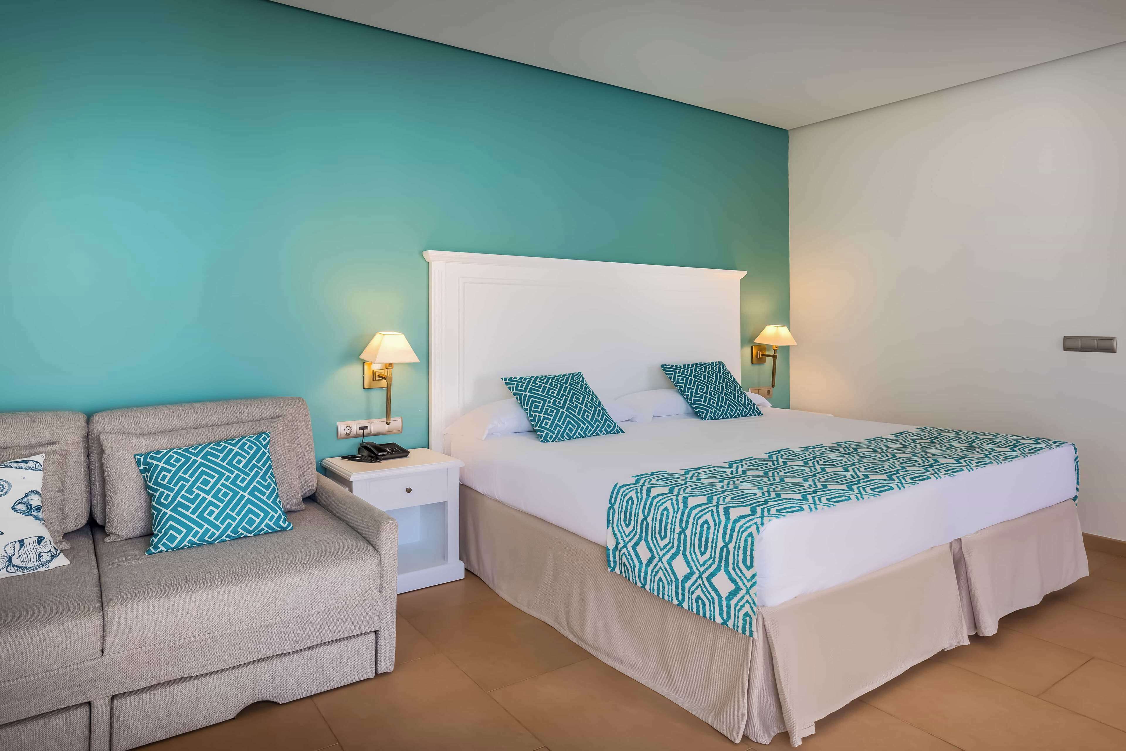 Un dormitorio ordenado con cama, sofá y dos mesitas de noche con lámparas.