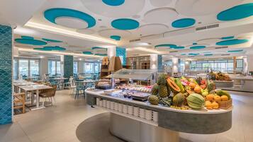 Un moderno comedor con una exhibición central de frutas, diseño de techo blanco y verde azulado, e iluminación natural proveniente de amplias ventanas.