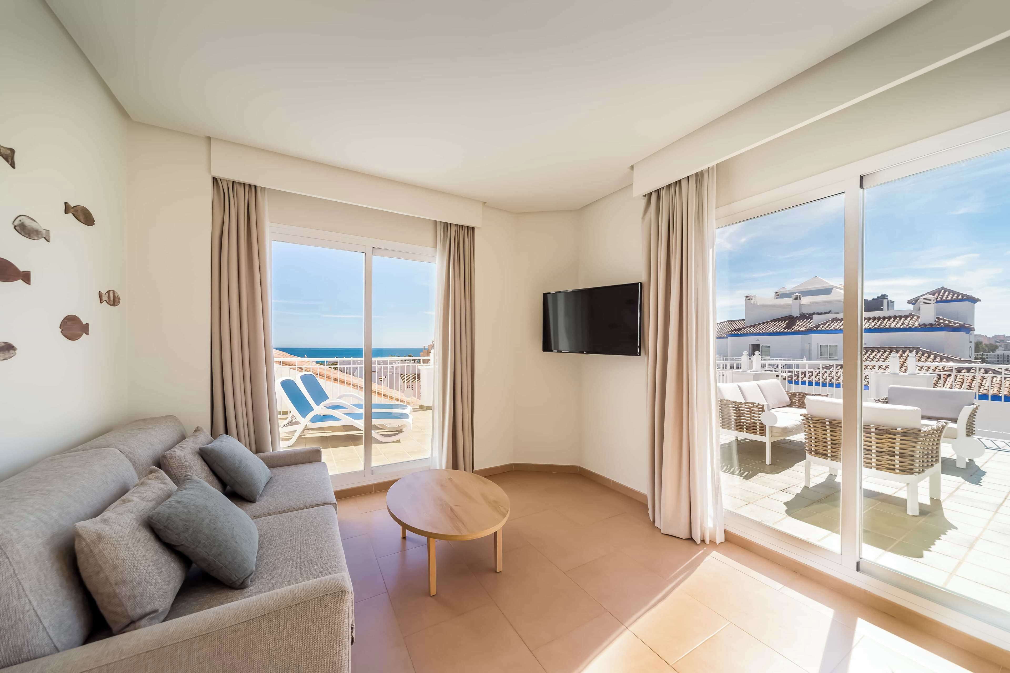 Une chambre d’hôtel moderne dotée d’un grand balcon, d’un canapé, d’une petite table et d’un téléviseur.