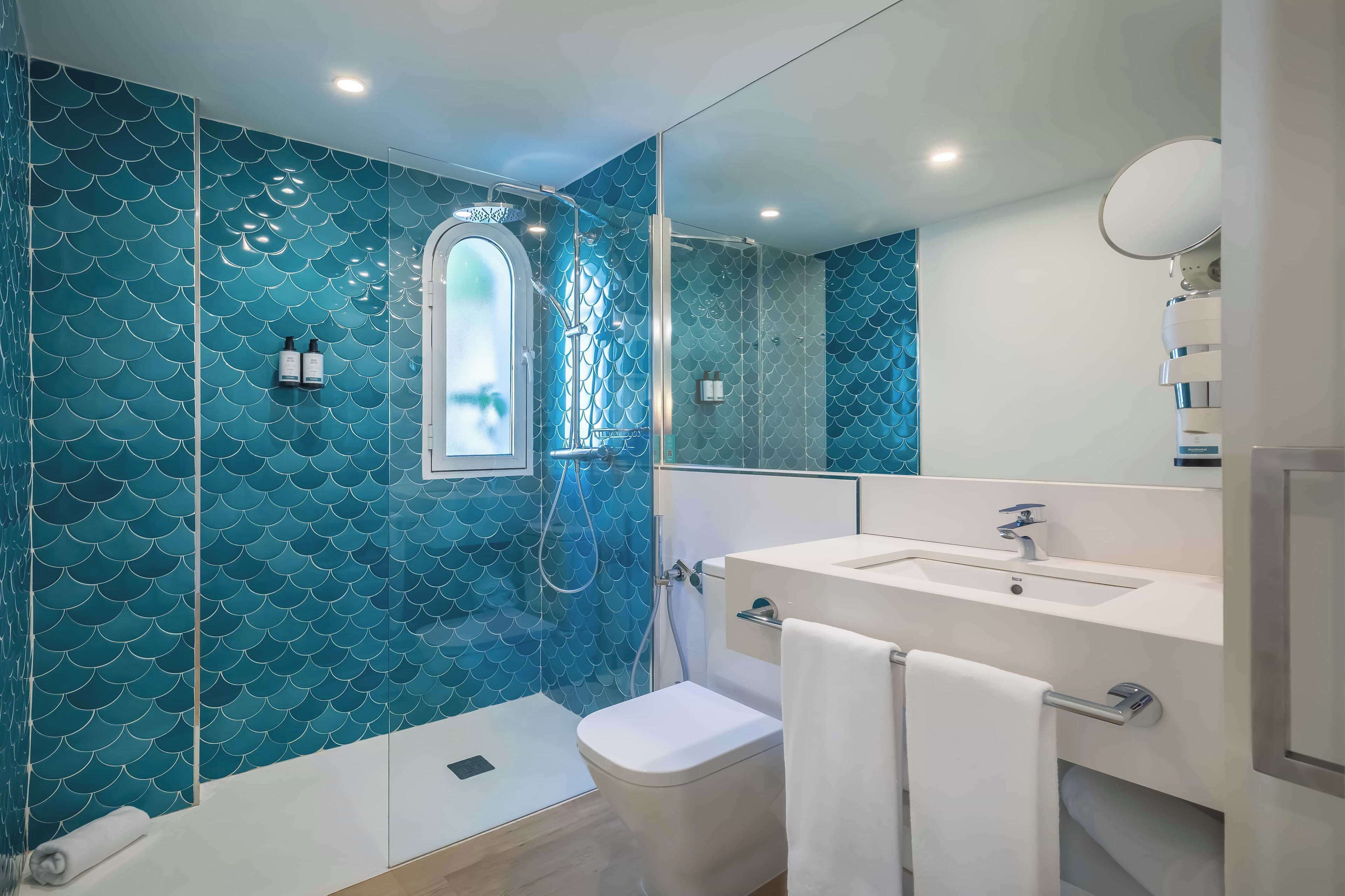 A bathroom with a blue tiled wall, a shower, a toilet, a sink, and a mirror.