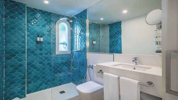 A bathroom with a blue tiled wall, a shower, a toilet, a sink, and a mirror.