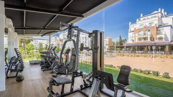 Un gimnasio con equipo de ejercicio diverso, un ventanal con vista a un edificio y una piscina.