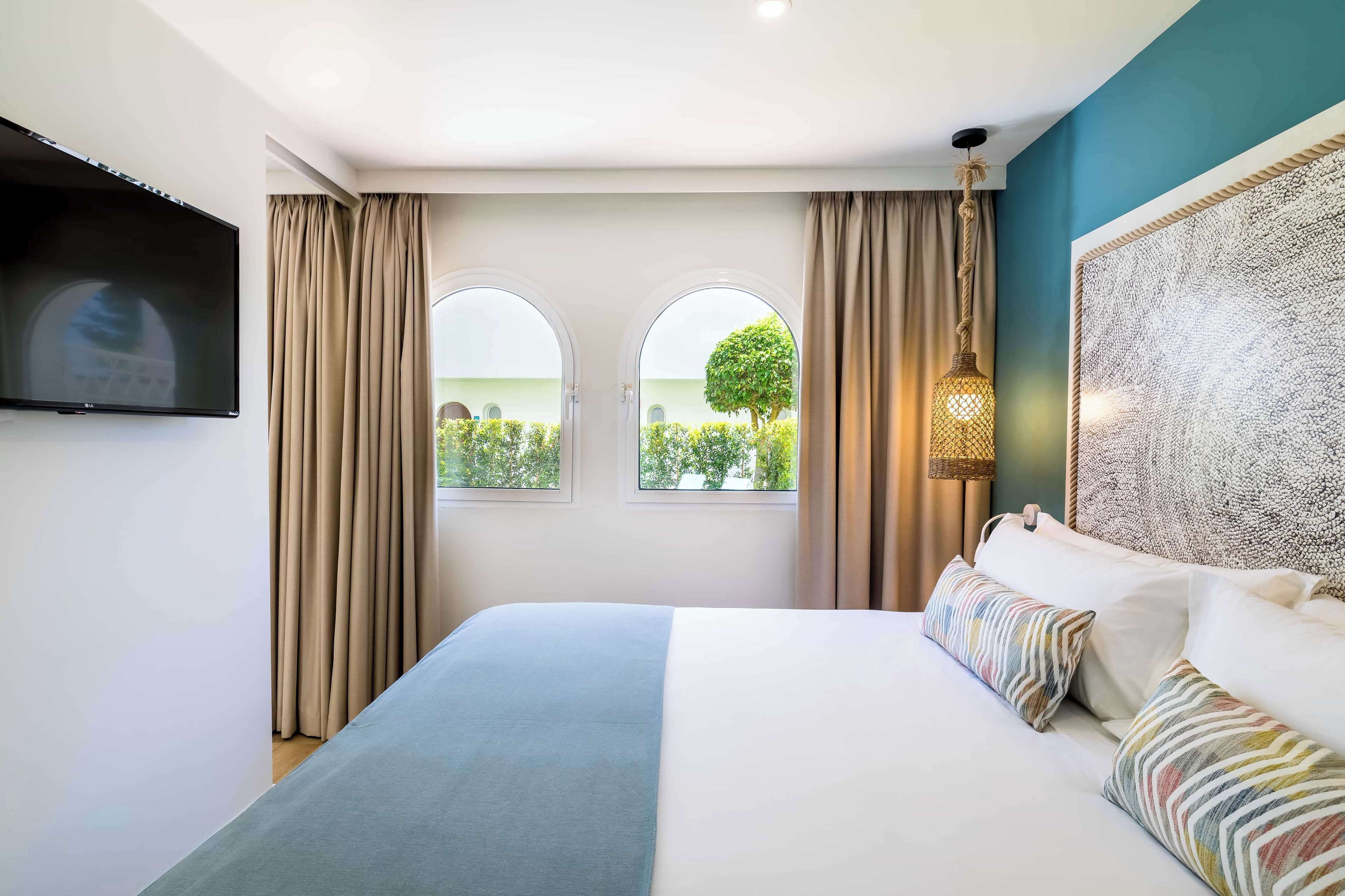 A bedroom with a bed, two windows, a TV, and a decorative wall piece.