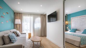 A modern hotel room with a sofa, a round table, a bed with a patterned bedspread, a flat-screen TV, and a large window with curtains.