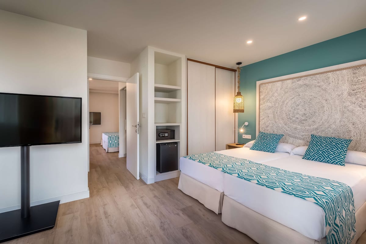 A bedroom with a bed, a TV, a wardrobe, and a small kitchenette.