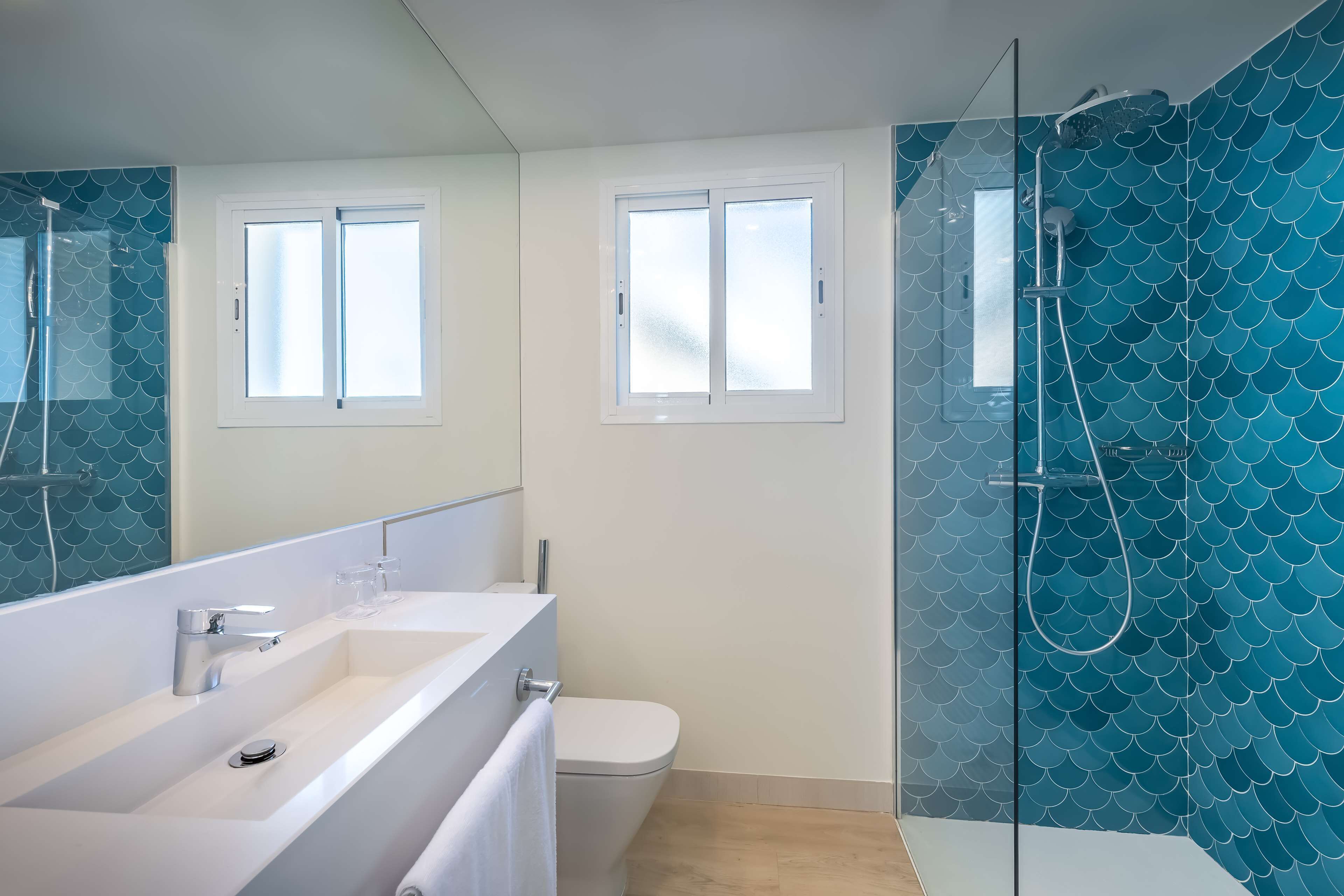 Un baño moderno con un espejo grande, dos lavamanos, inodoro y cabina de ducha con mampara de vidrio.