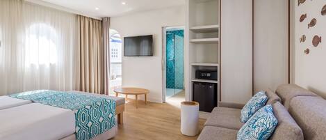 A modern hotel room with a bed, a sofa, a TV, a small table, and a bathroom with a shower.