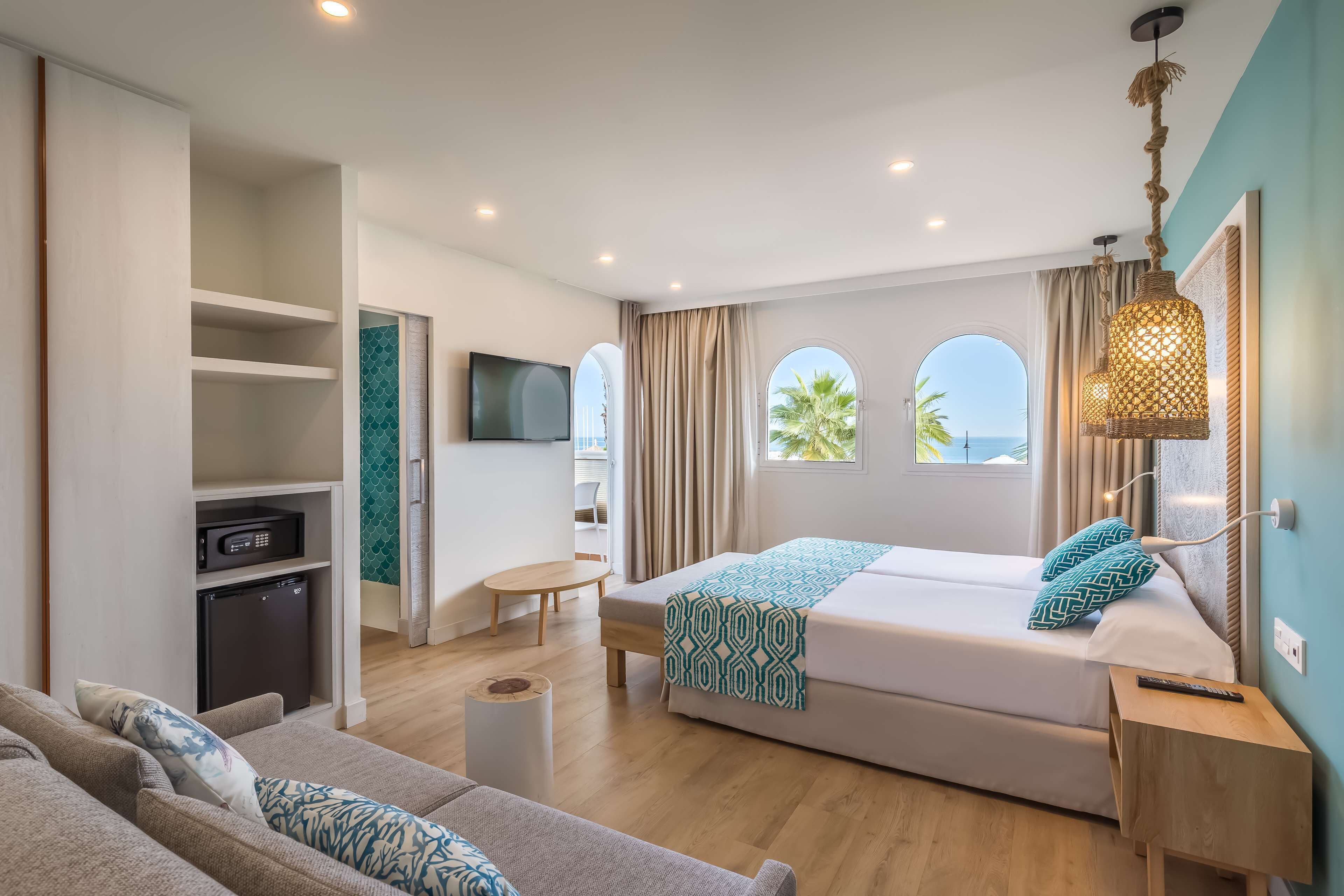 Una habitación de hotel moderna con cama, sofá, televisión y una pequeña kitchenette.