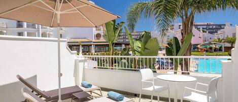 A balcony with a pool, lounge chairs, and a table with chairs.