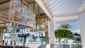 Un bar moderno con letrero de neón, asientos exteriores y vista a la piscina.