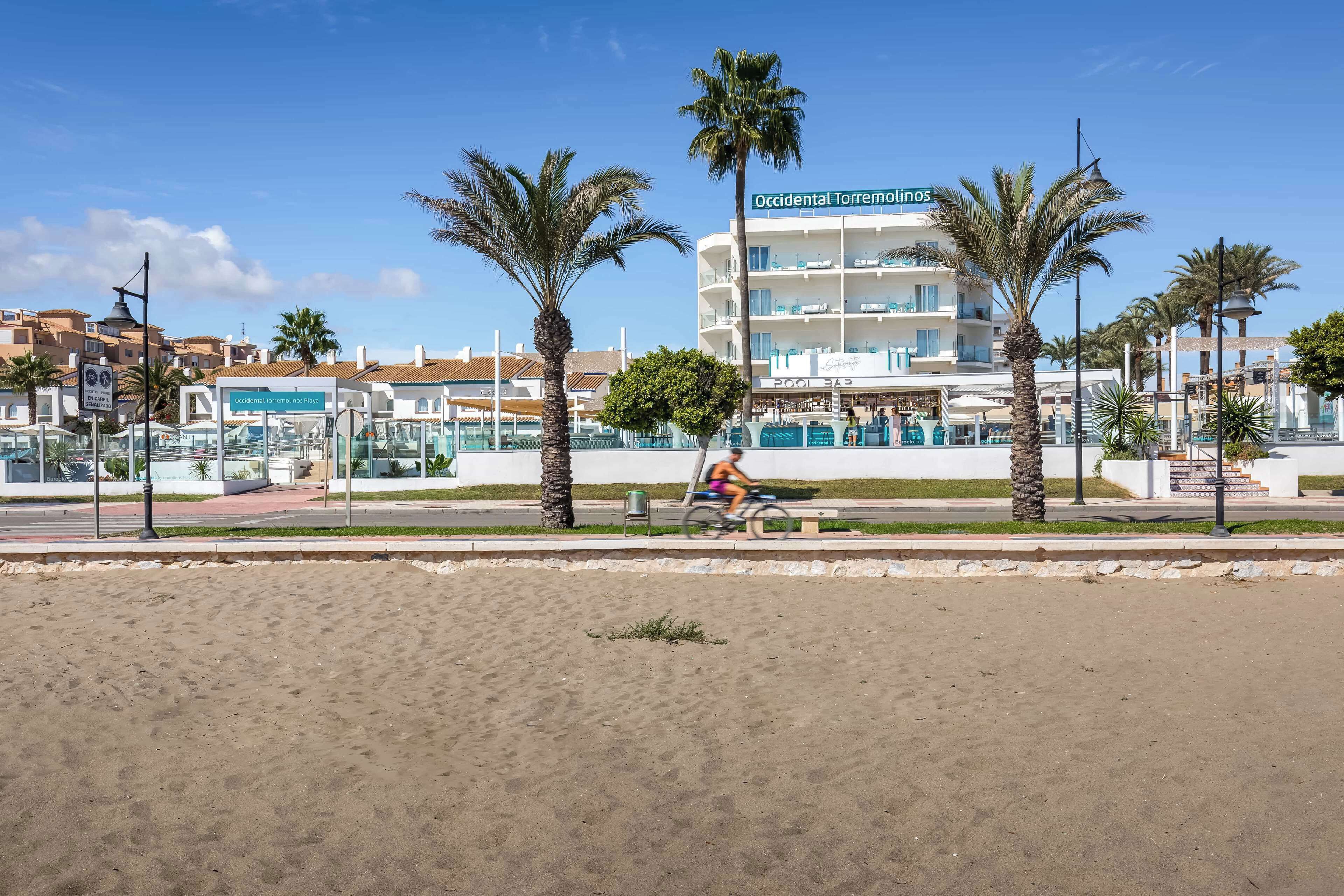 A coastal hotel with a pool area, palm trees, and a clear blue sky.