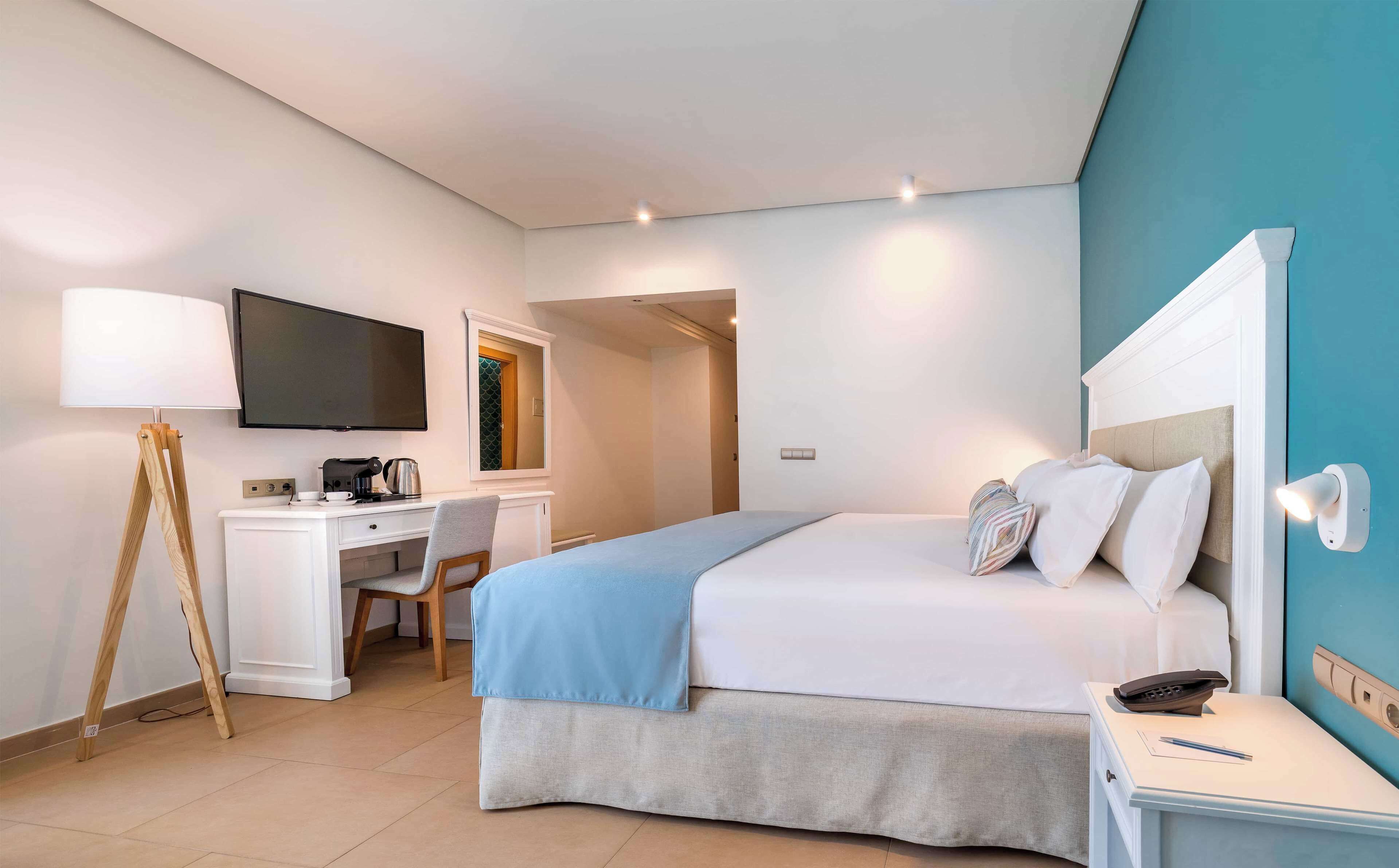 A hotel room with a bed, a desk with a lamp, a television, and a bathroom visible through an open door.