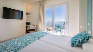 Habitación de hotel con cama, televisión, silla y balcón con vistas.