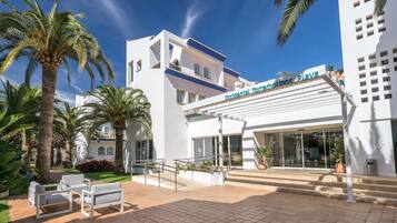 A modern hotel with a white facade, palm trees, and a clear blue sky.