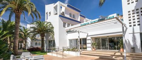 Un hotel moderno con fachada blanca, palmeras y un cielo azul despejado.