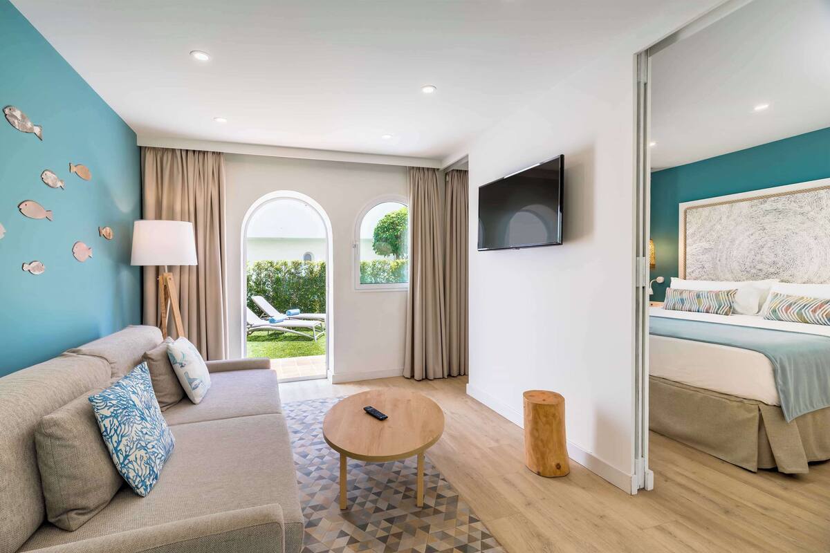 A modern hotel room with a sofa, a round coffee table, a bed, and a TV mounted on the wall.