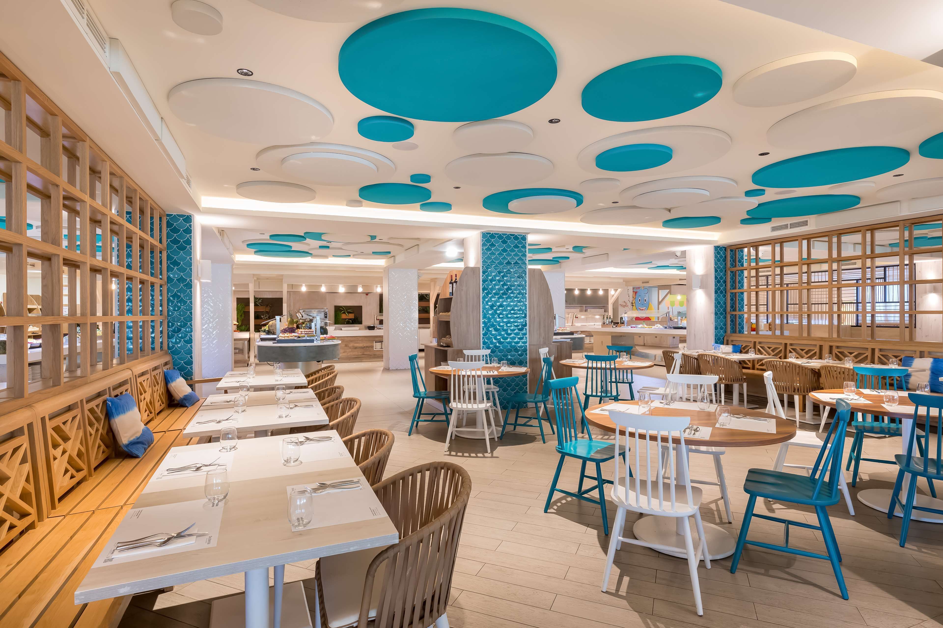 A modern restaurant interior with round tables, blue chairs, and a wooden partition wall.