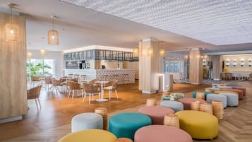 Un amplio vestíbulo de hotel con piso de madera, zonas de estar coloridas y un área de bar central con techo estampado.