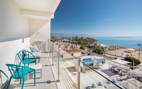 A balcony with turquoise chairs, a white sofa, and a view of the beach and ocean.