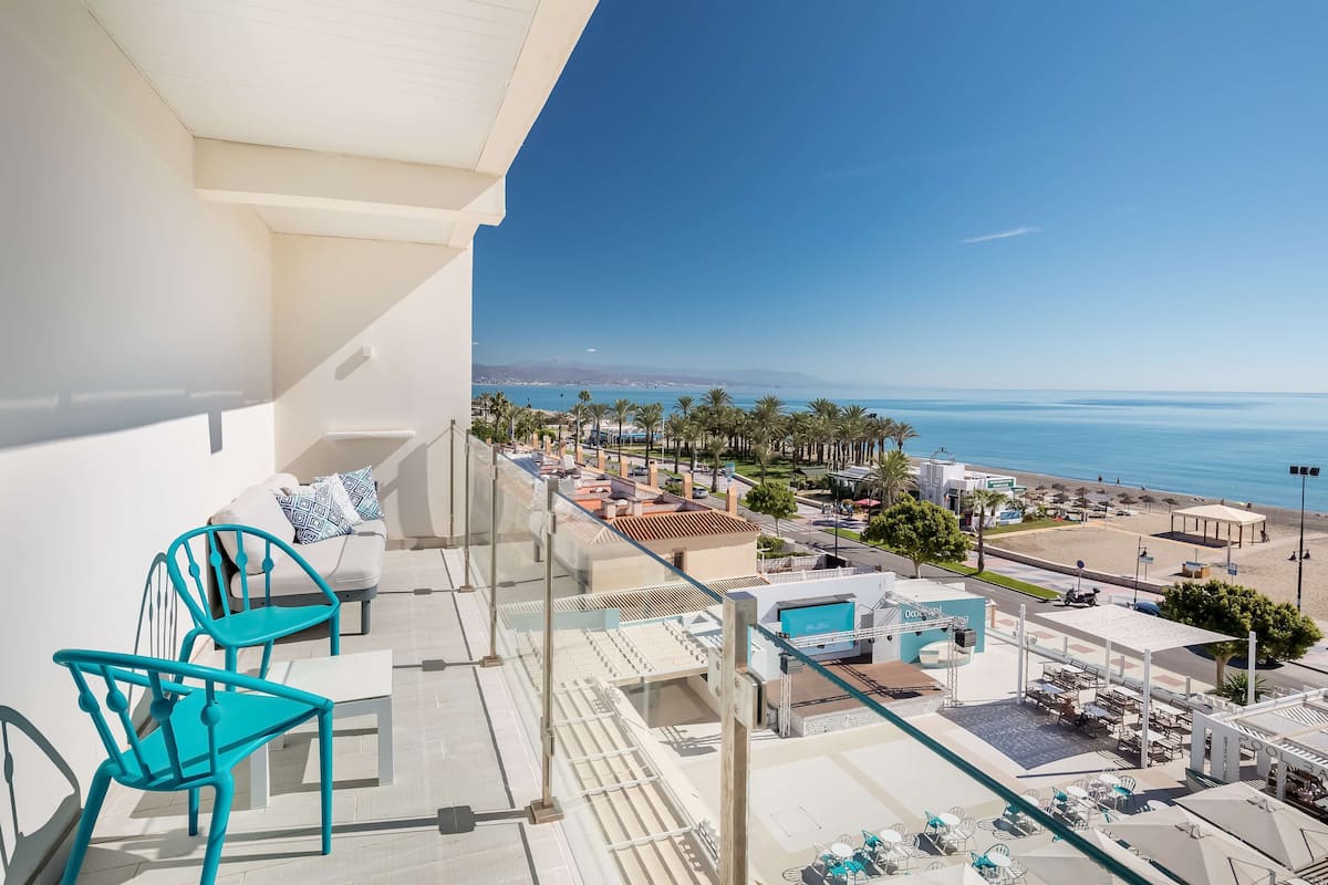 A balcony with turquoise chairs, a white sofa, and a view of the beach and ocean.
