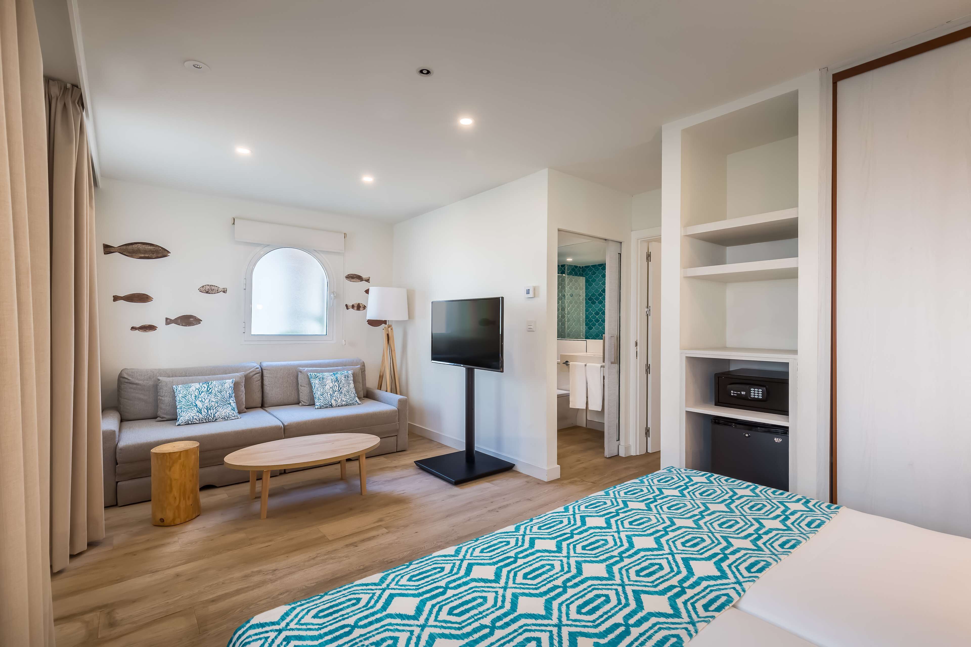 A modern hotel room with a sofa, TV, and a patterned bedspread.