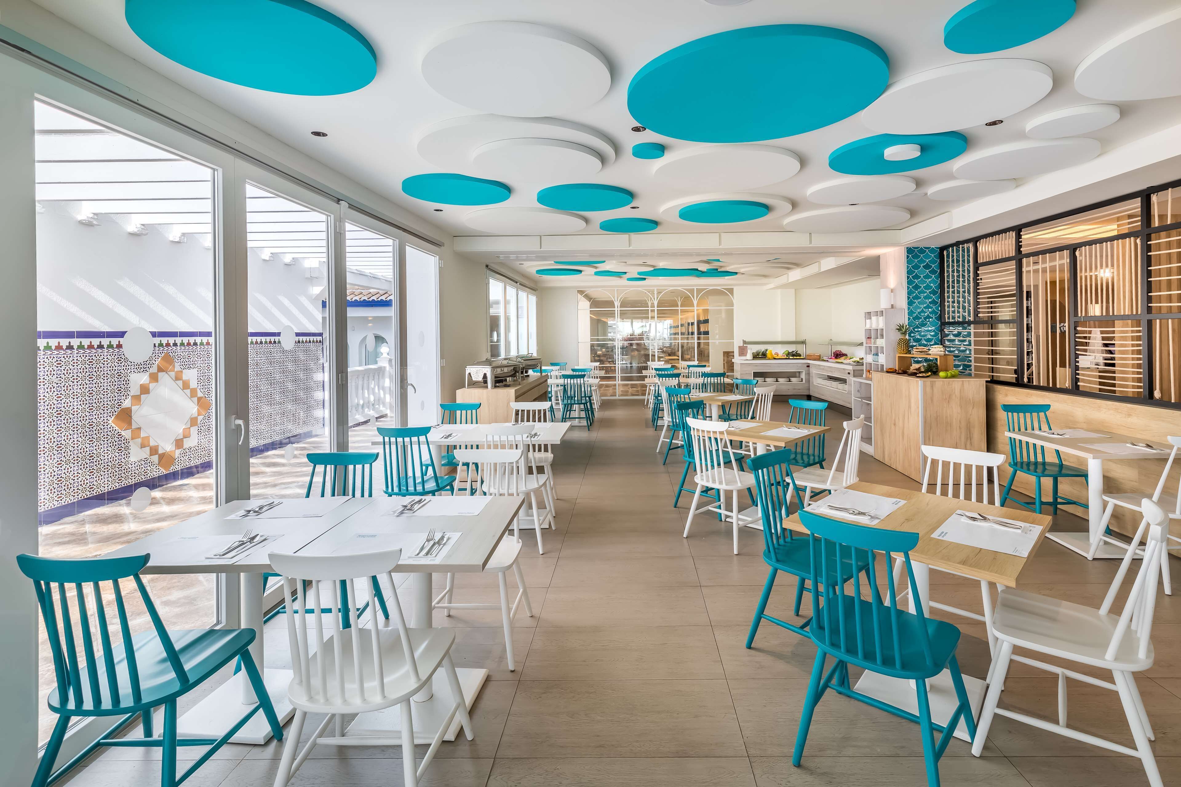 Un vaste espace dédié à la salle à manger, avec des chaises blanches et turquoise, un long comptoir et un design moderne au niveau du plafond.