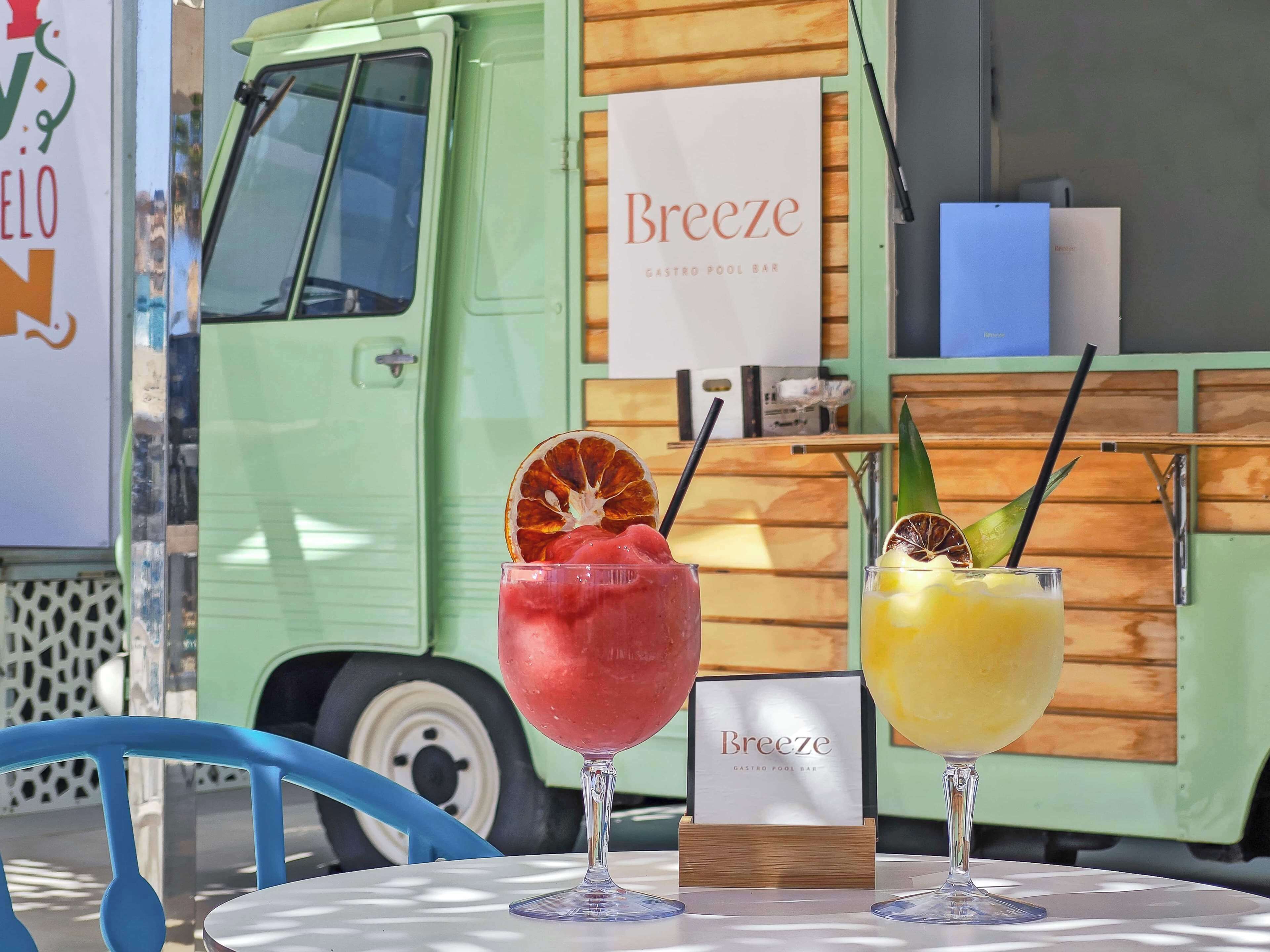 Two drinks on a table with a sign for 'Breeze Gastro Pool Bar' in the background.