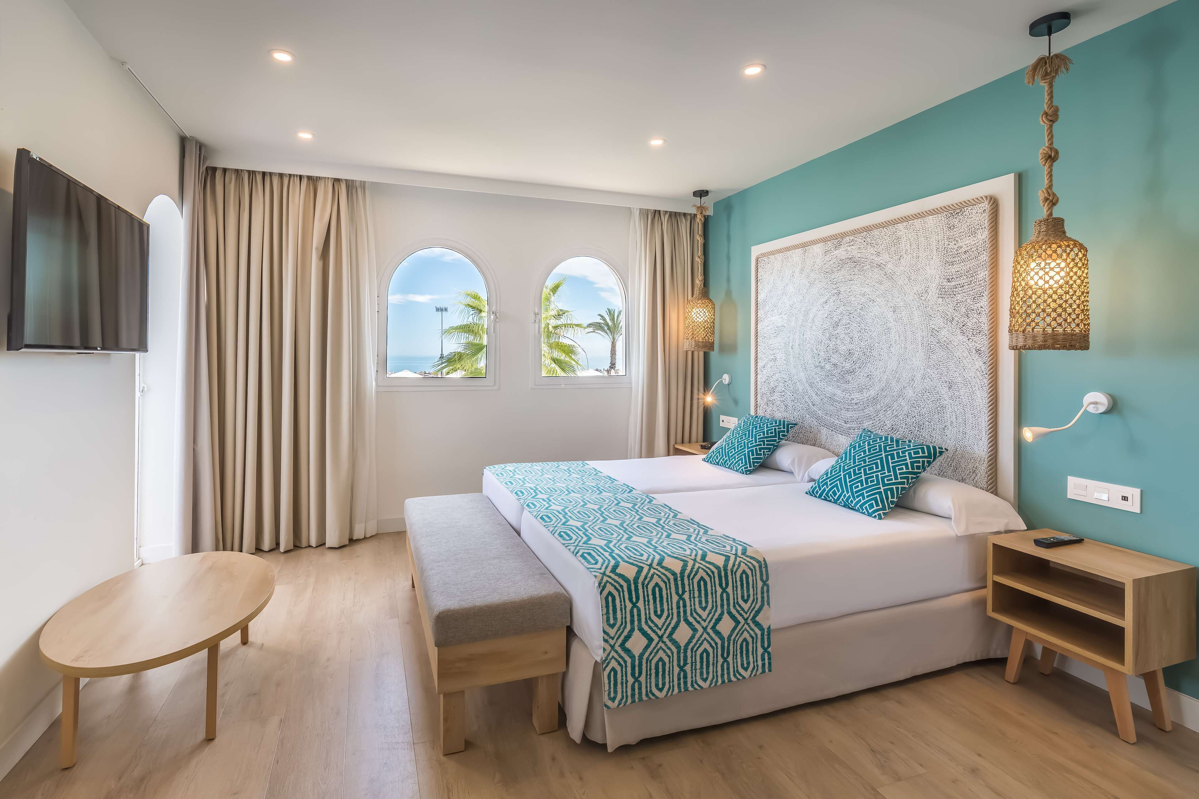 A modern bedroom with a large bed, a bedside table, a bench, and a TV mounted on the wall.