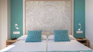 A double bed with a patterned bedspread, two matching pillows, a textured headboard, bedside lamps, and a nightstand with a phone.