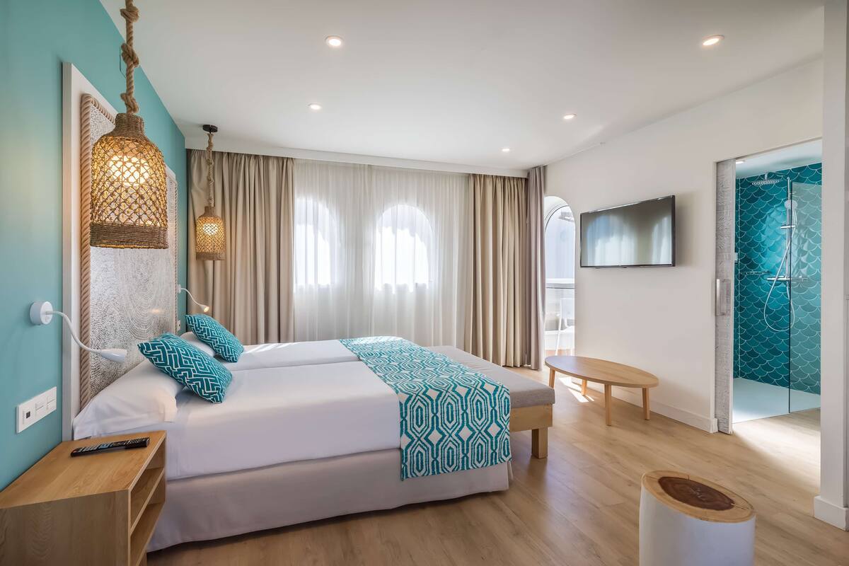 A modern hotel room with a large bed, a bedside table, a TV, and a bathroom with a shower.