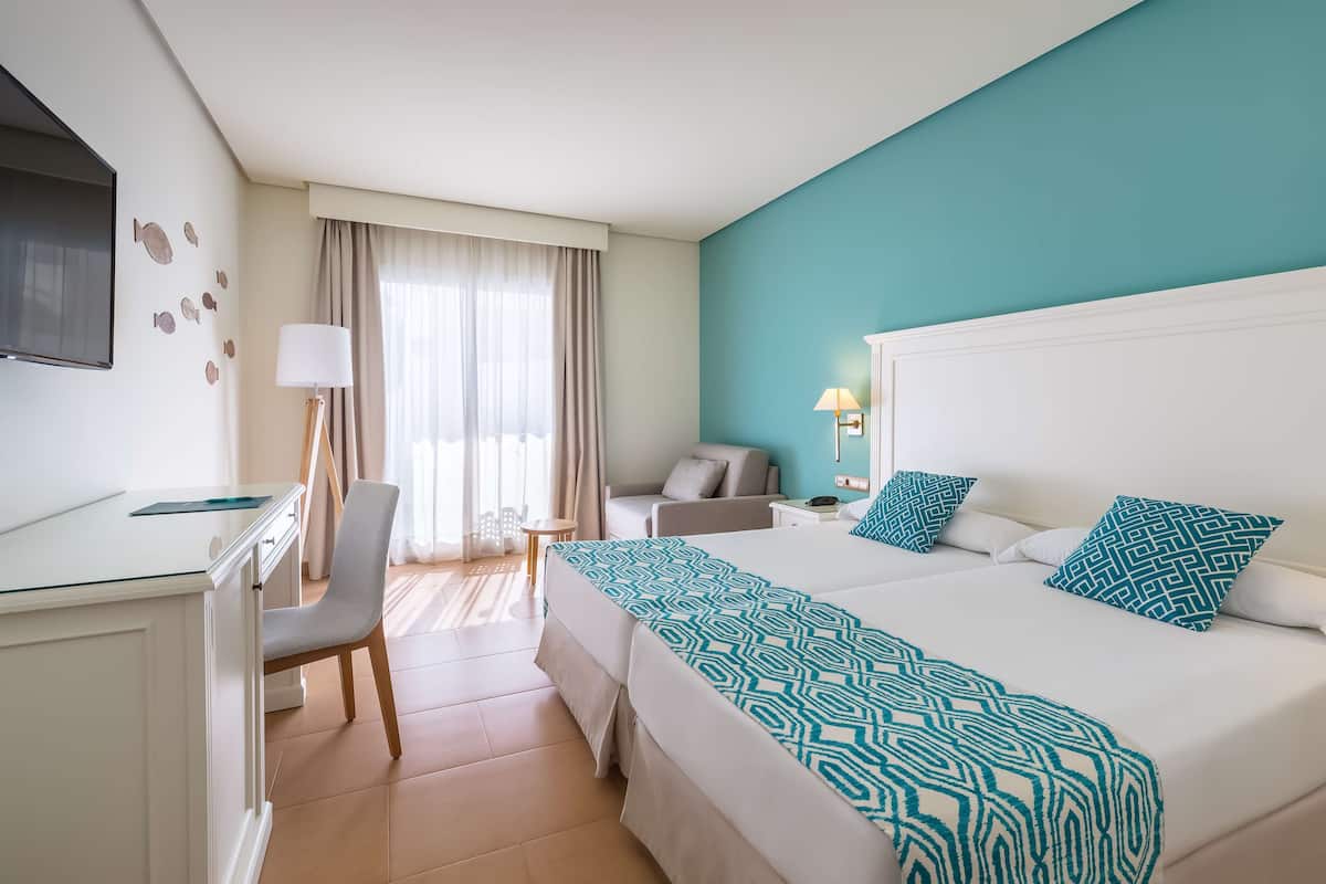 A hotel room with a bed, a desk, a chair, a TV, and a window with curtains.