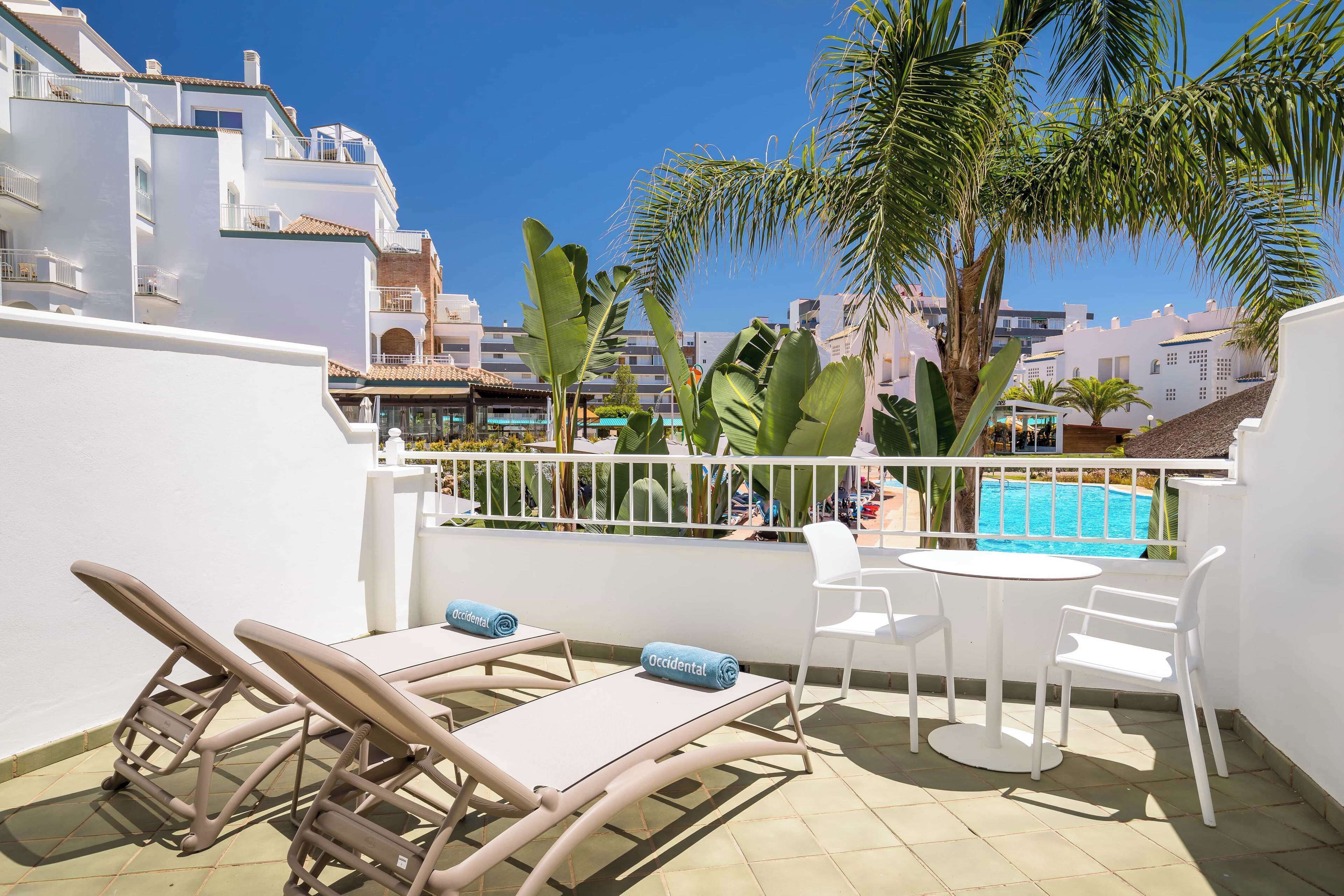 A rooftop terrace with a pool, white walls, and tropical plants.