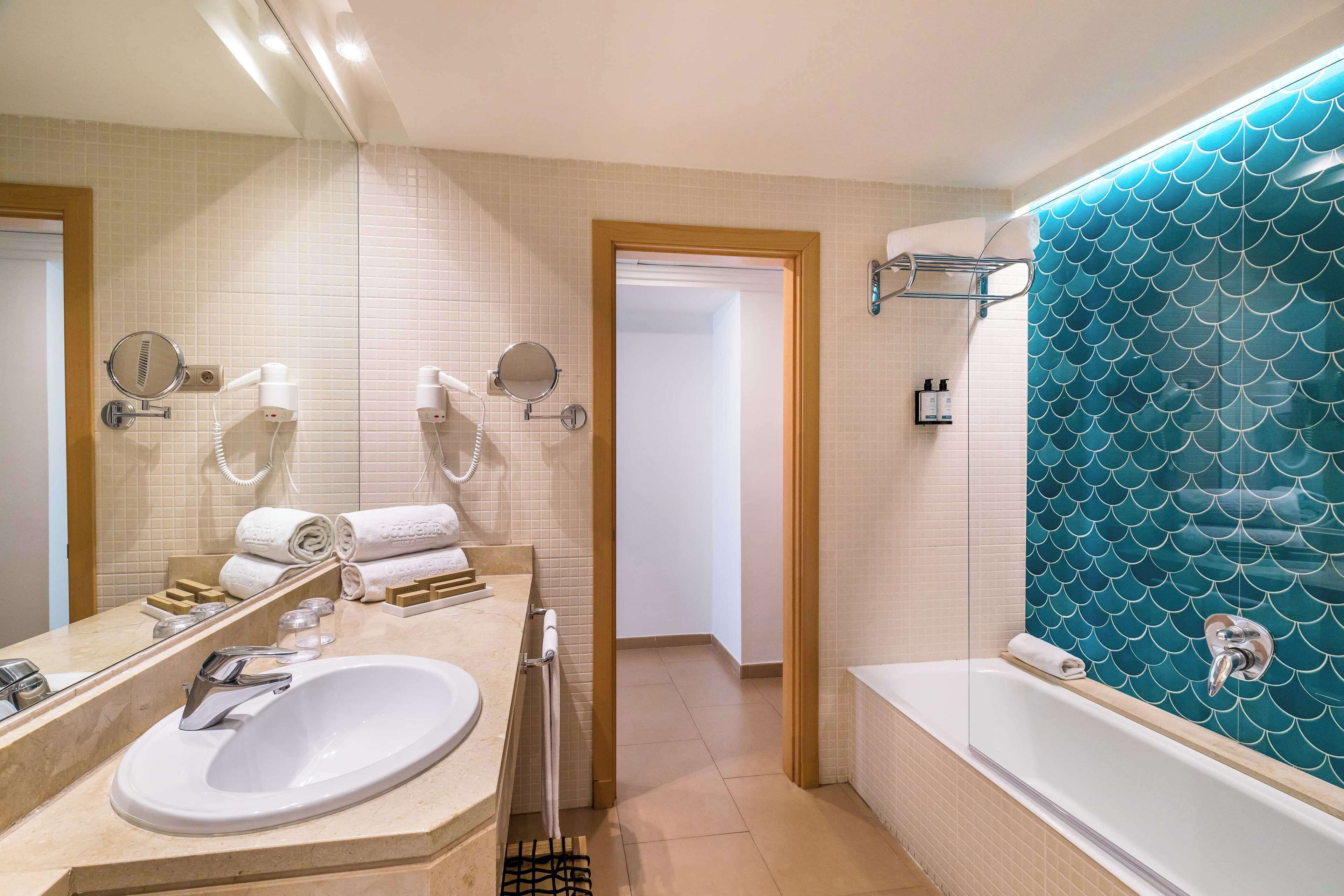 A bathroom with a white sink, a mirror, a towel rack, and a bathtub with a blue tiled wall.