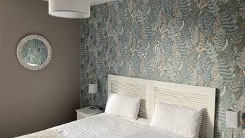 Une chambre à coucher avec un lit, deux tables de chevet, une lampe, un miroir fixé au mur et un papier peint à motifs.