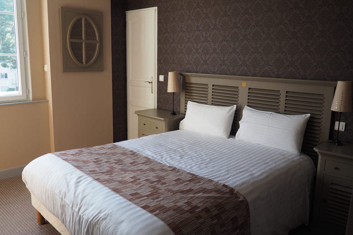 Una cama bien hecha con ropa de cama blanca y marrón, un cabecero de madera y dos lámparas de noche.