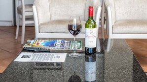 A kitchen with a granite countertop, a wine bottle, and a glass of red wine. There are two white chairs and a dining table in the background.