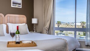 A hotel room with a bed, a wine bottle, and a tray with a glass of wine.