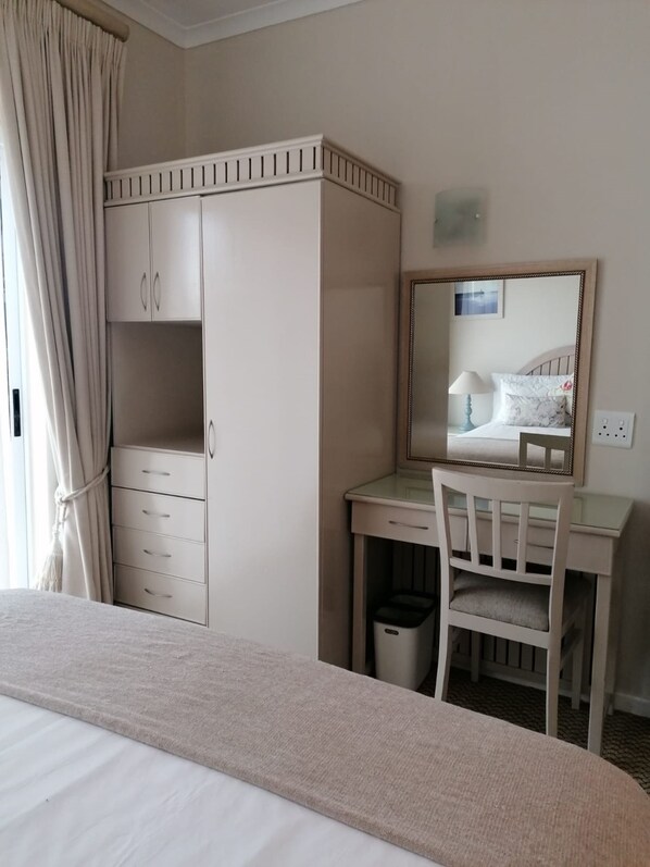 Une chambre d’hôtel comprenant un lit, un bureau avec une chaise, une armoire et un miroir.