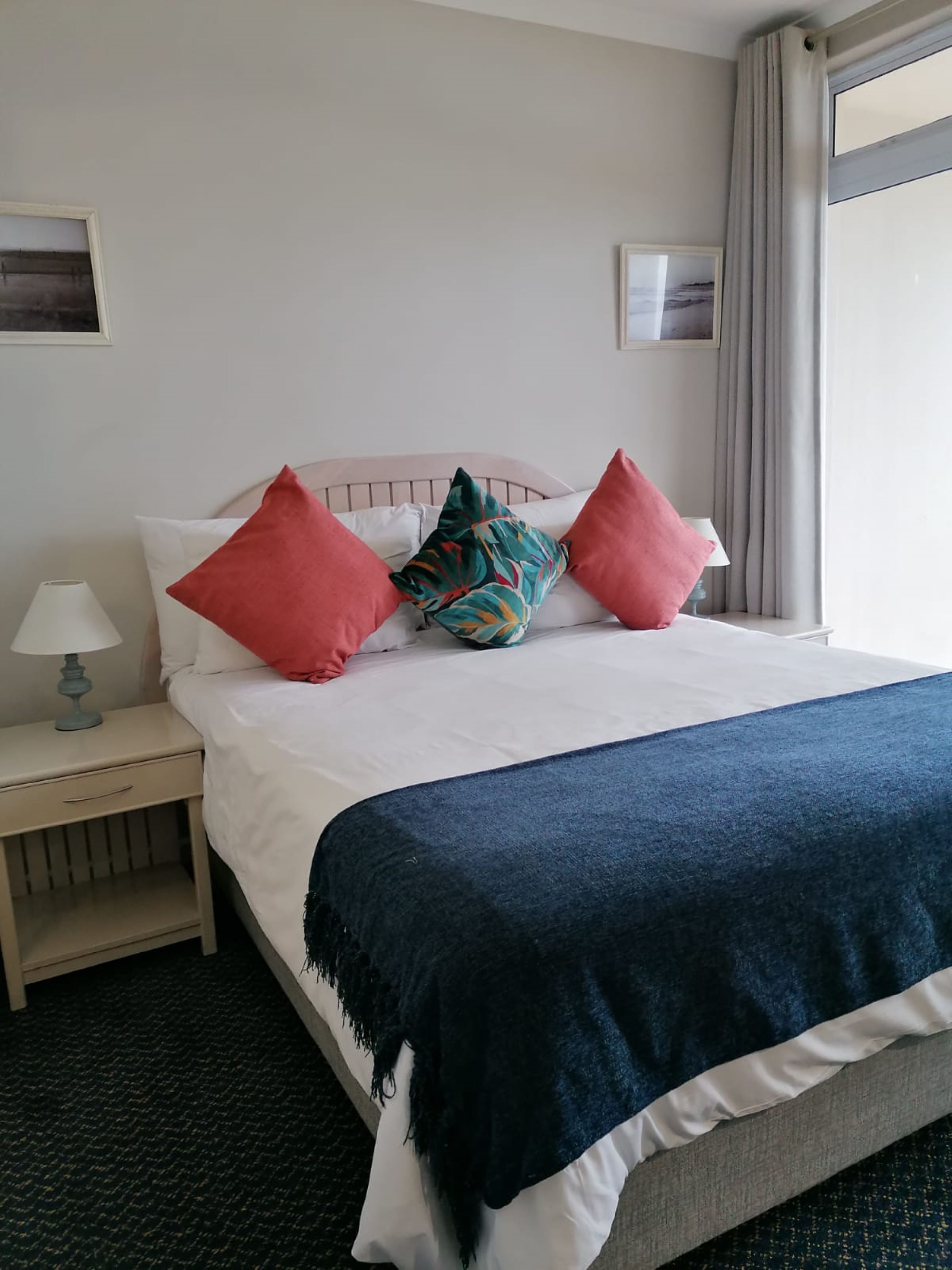A hotel room with a bed, a nightstand, a lamp, and a window with curtains.