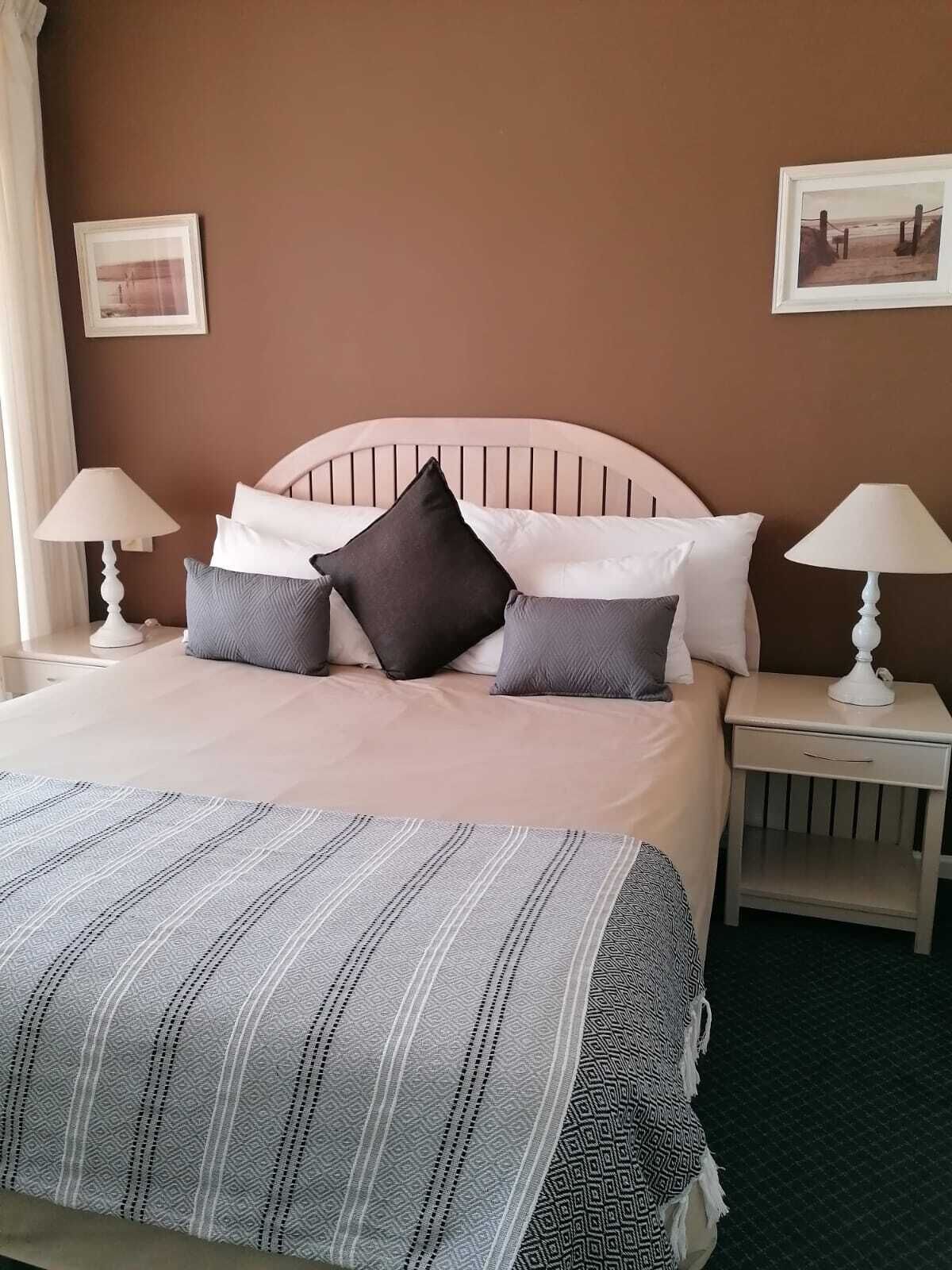 A neatly made bed with a striped bedspread, two bedside tables with lamps, and two framed pictures on the wall.