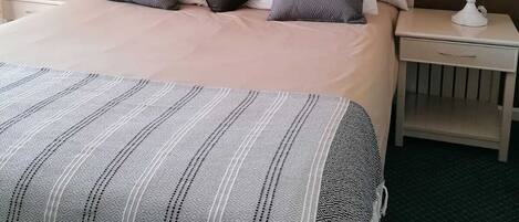Una cama bien hecha con una colcha a rayas, dos mesitas de noche con lámparas y dos cuadros en la pared.
