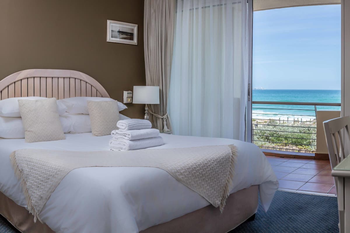 Een hotelkamer met een bed, uitzicht op de oceaan, een stoel en een tafel.
