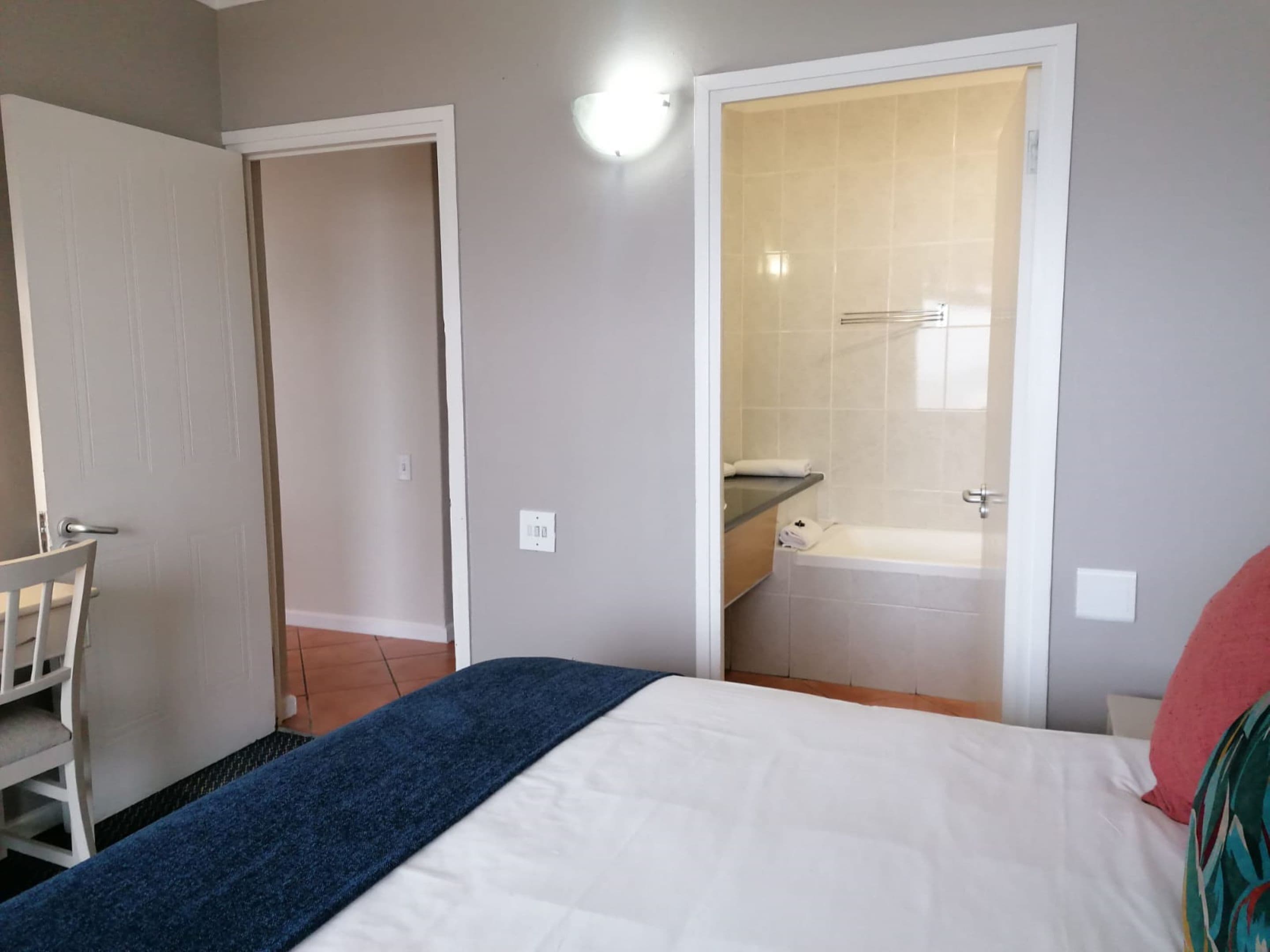 A bedroom with a bed, a chair, a bathroom with a bathtub, and a door leading to another room.