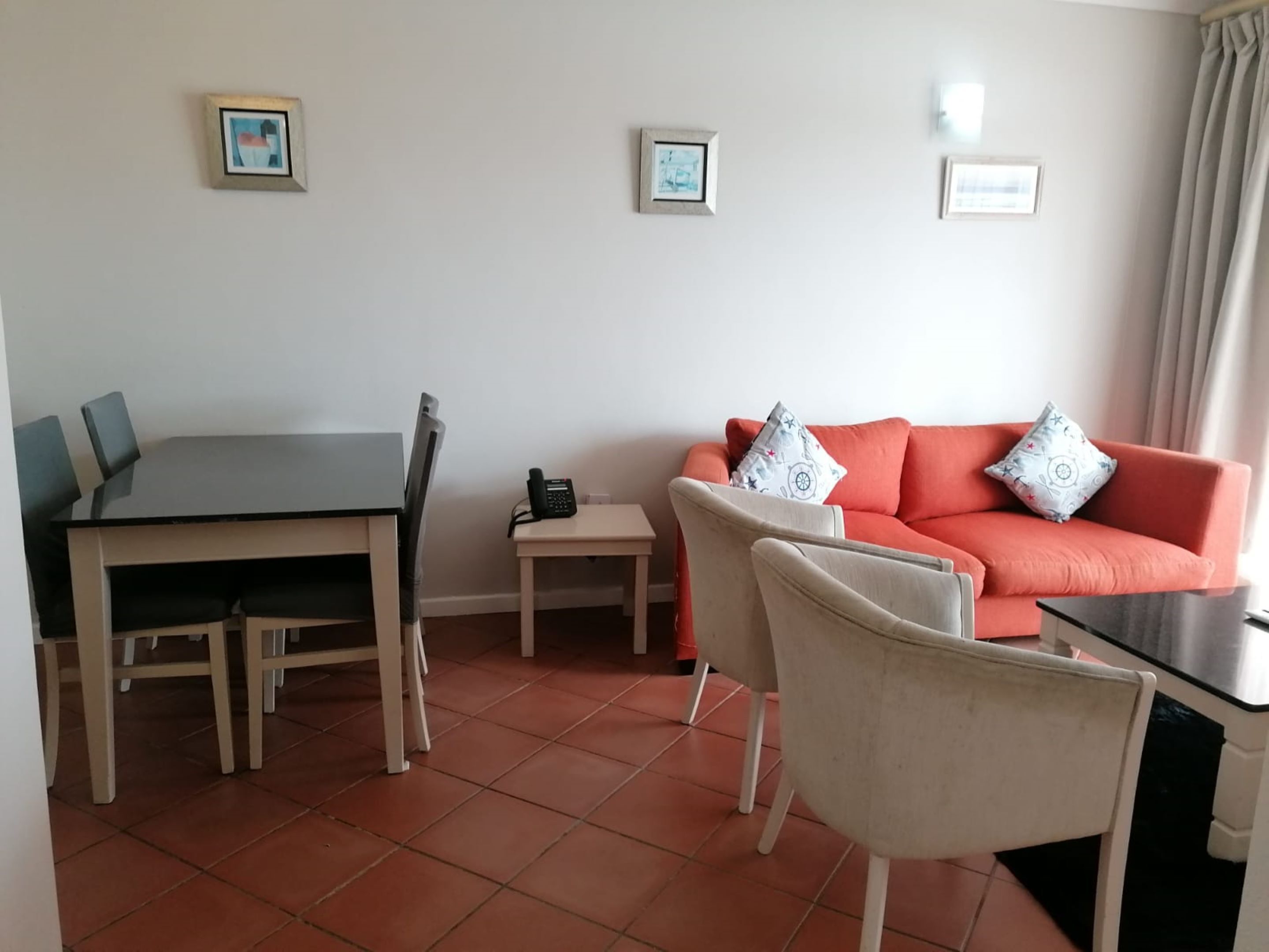 Una sala de estar con una mesa de comedor, sillas, un sofá con cojines estampados y una pequeña mesita auxiliar.