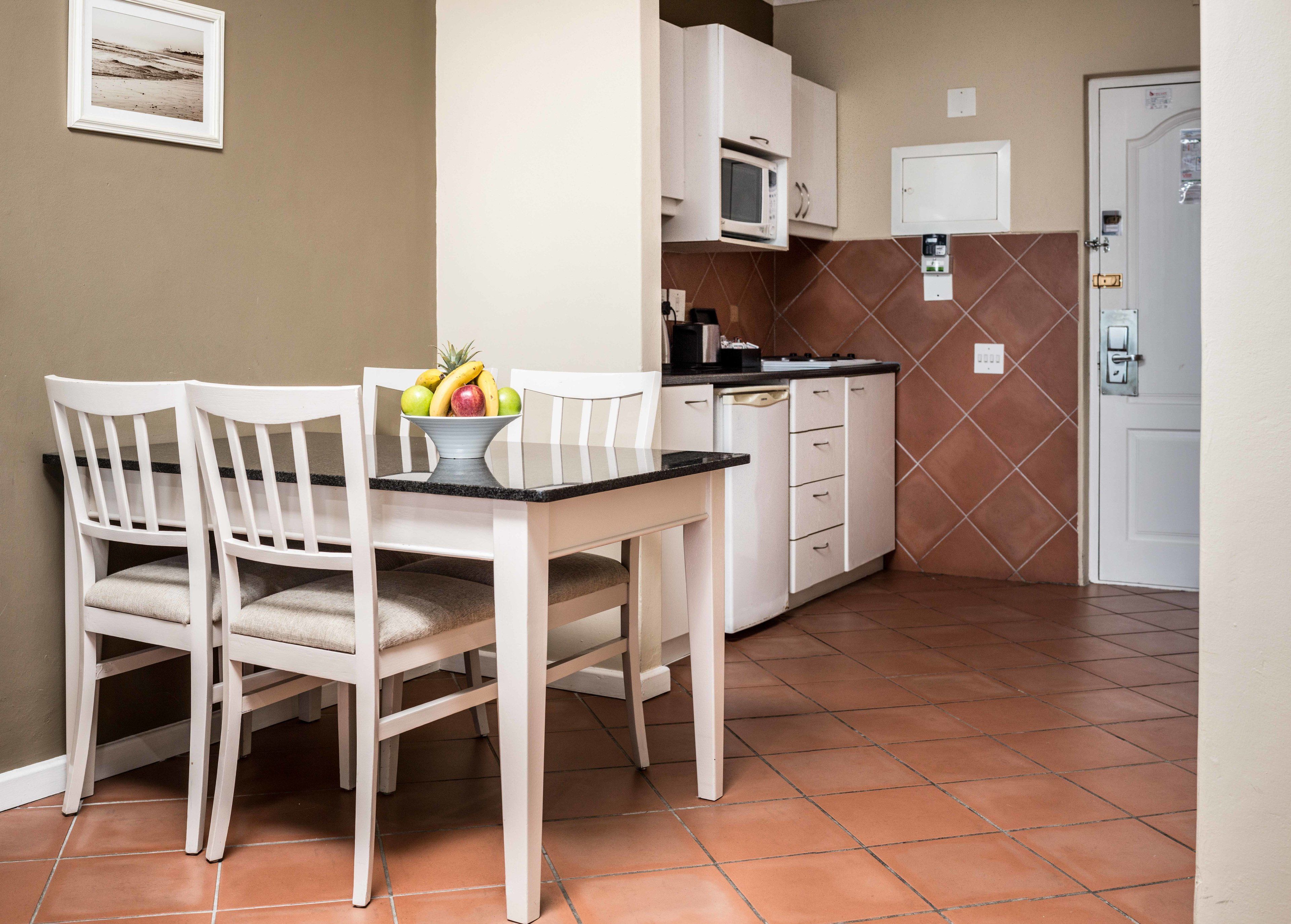 Una piccola cucina con mobili bianchi, un forno a microonde e un tavolo da pranzo con sedie.