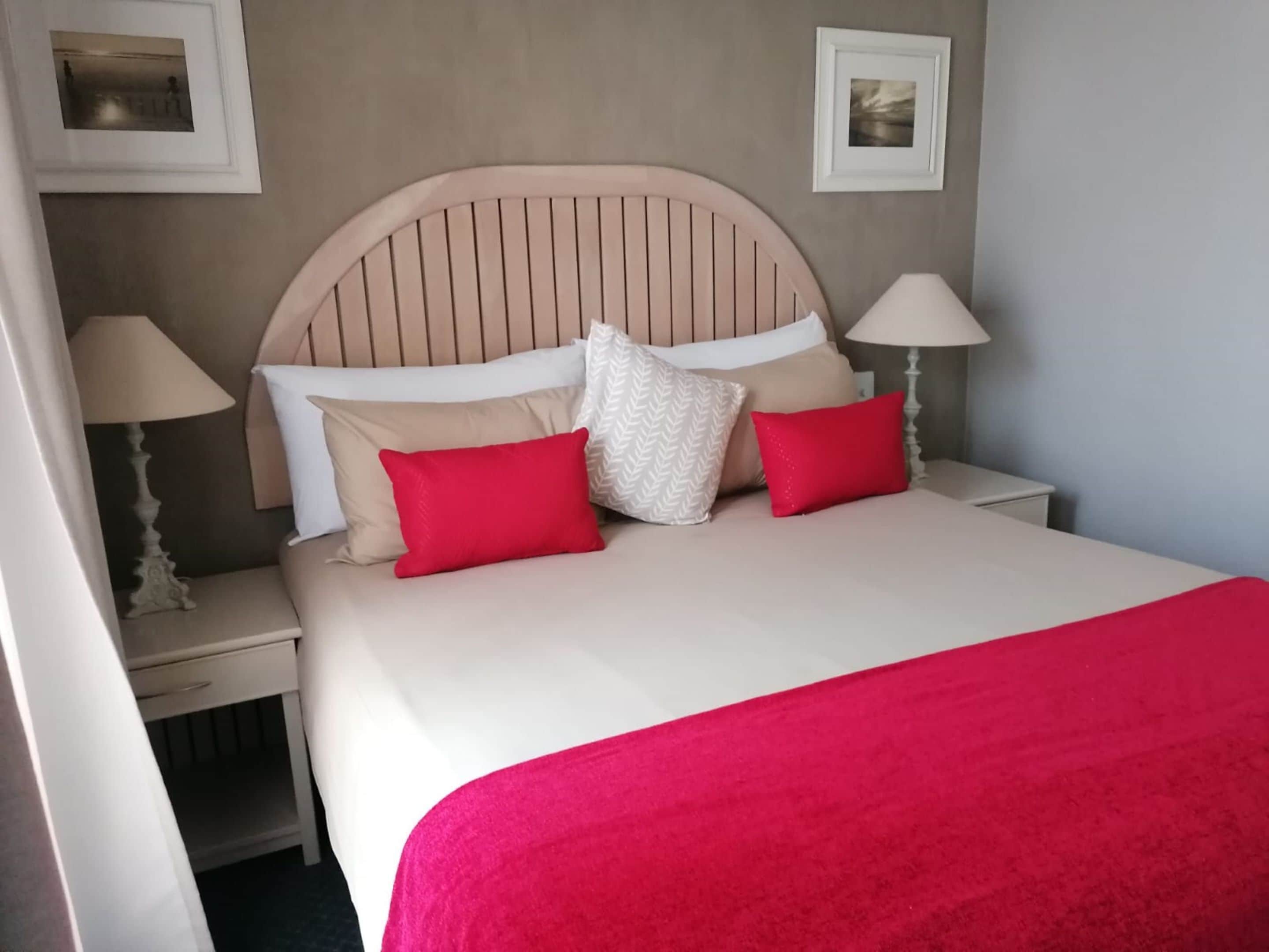 A neatly made bed with a headboard, two bedside lamps, and a red throw blanket.