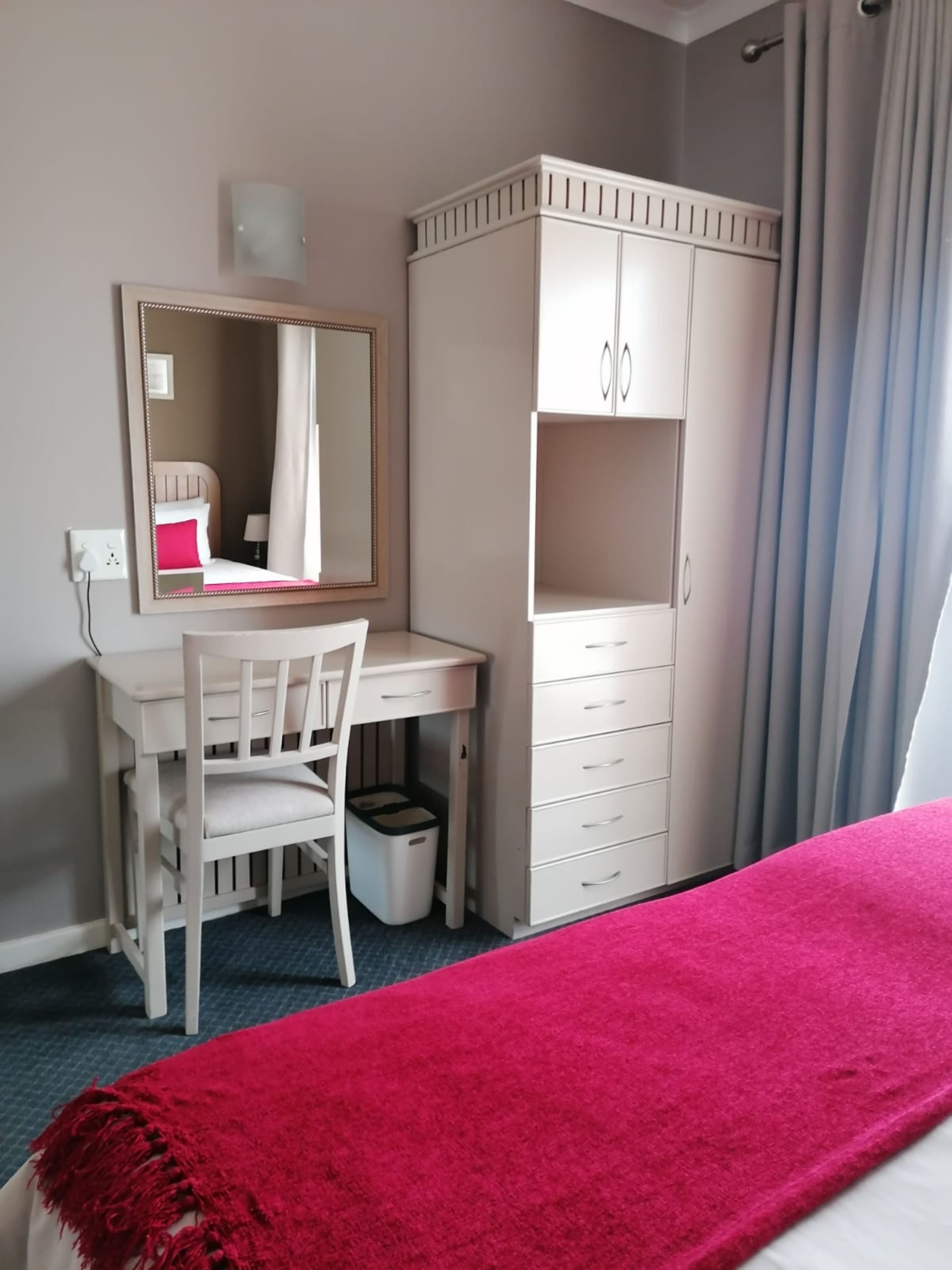 A bedroom with a bed, a desk, a chair, a wardrobe, and a mirror.