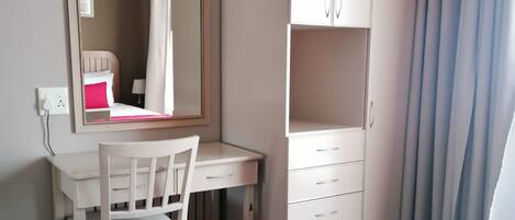 A bedroom with a bed, a desk, a chair, a wardrobe, and a mirror.